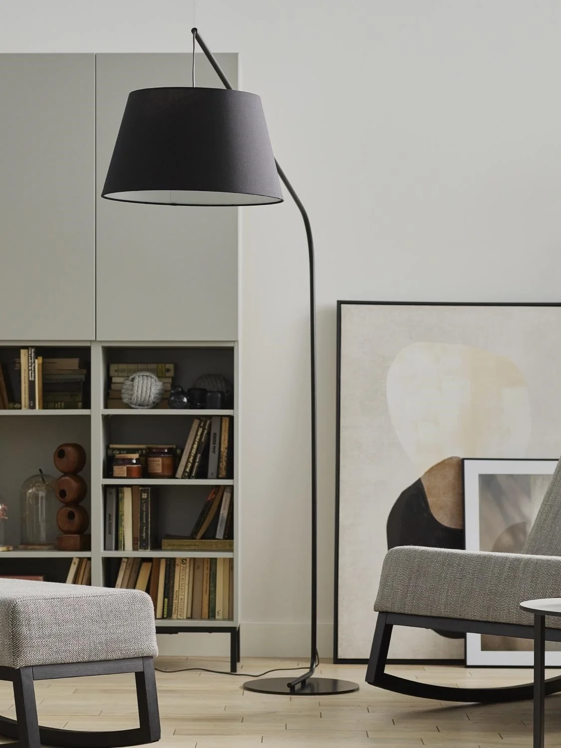 Czarna, minimalistyczna lampa podłogowa w salonie, obok regału z książkami .
